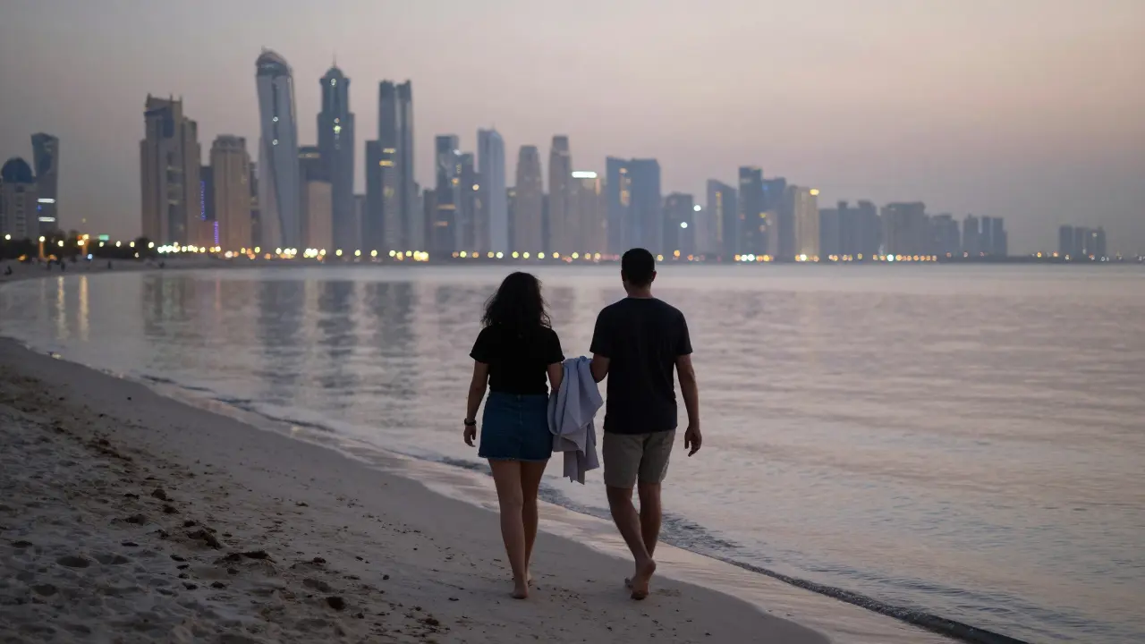 Two people walking barefoot on Jumeirah Beach at dusk, city lights reflecting on calm water.